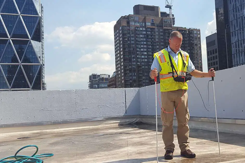Contractor performing wet testing electronic roof leak detection on a flat roof